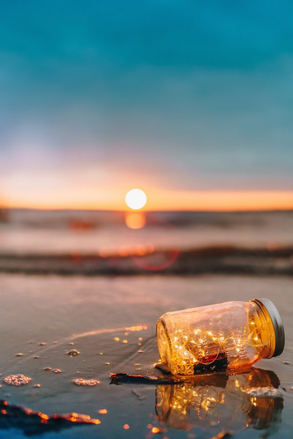 What is gold used for? Empty jam jar left on a beach after the tide has gone out. Golden yellow sun rising in background.