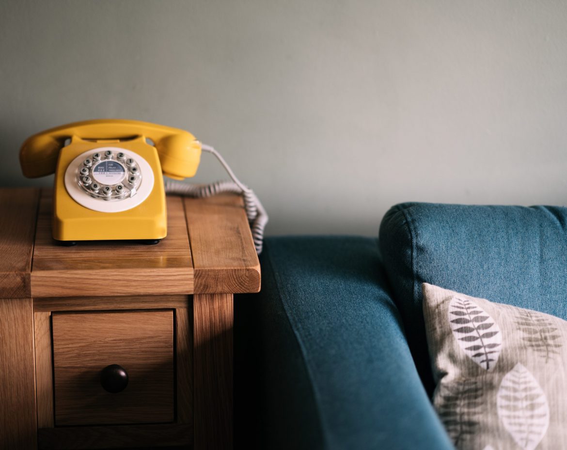 Investment scams: Living room scene, dominated by blue sofa with yellow phone sitting on a wooden side locker