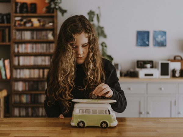 B Corps: Young girl placing a coin into a money box in the shape of a surf bus