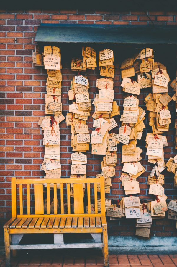 Retirement planning: An empty yellow bench leaning against a red brick wall with a bunch of messages and cards hanging from it