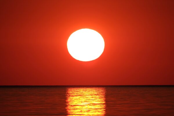 Hummingbird Resources HUM Share Price News: Sun setting against a red sky overlooking the sea