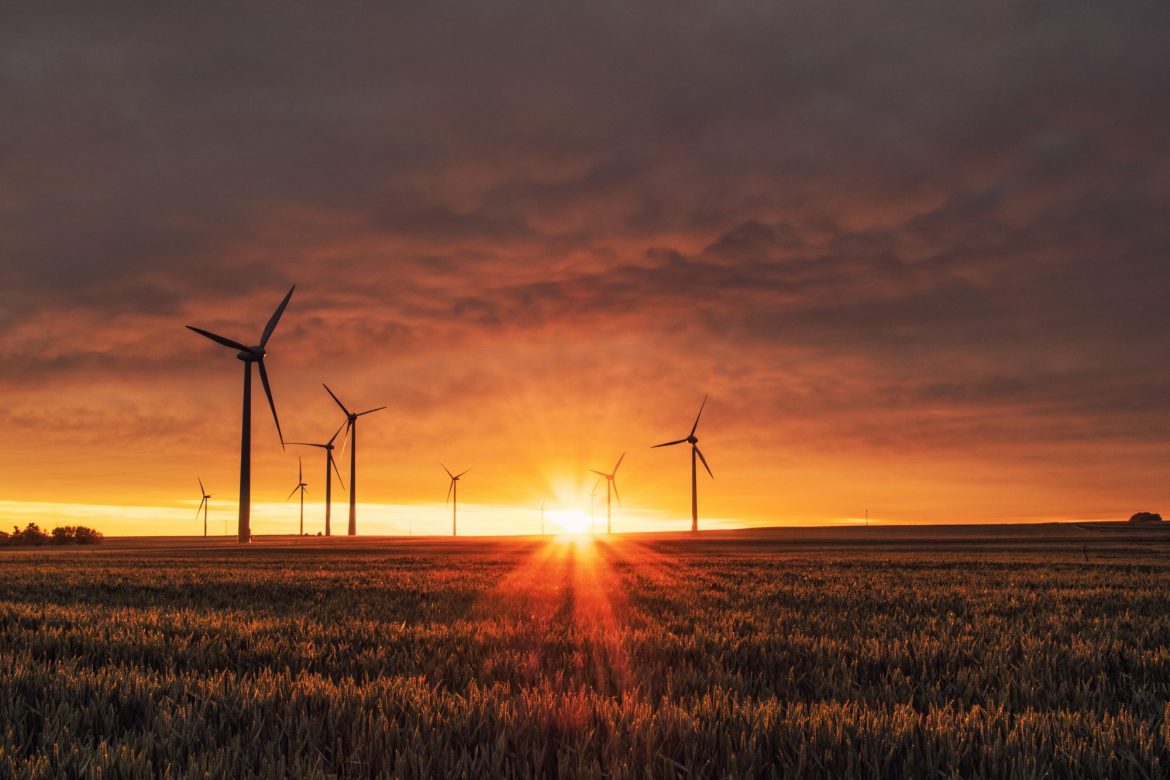 Renewable energy investment: Several windmills dotted across the landscape with the sun shining through
