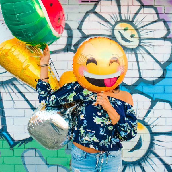 Money management apps: woman surrounded by helium balloon with a smiley face one covering here face
